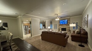 A modern living room with a brown leather sofa, a flat-screen TV, and a fireplace. - Fountain Hills Grandeur (Lubbock)