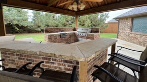 An outdoor barbecue area with a brick grill, a ceiling fan, and a table with chairs. - Fountain Hills Grandeur (Lubbock)