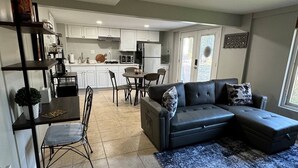 A modern living room with a grey sectional sofa, a dining table with chairs, and a kitchen in the background. - Stylish 1BR Near Tysons, Wolf Trap & Metro Access (Tysons)
