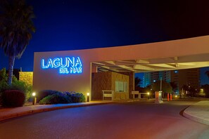 L’entrée d’un hôtel, illuminée par une enseigne au néon sur laquelle on peut lire « LAGUNA DEL MAR », de nuit.