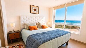 Une chambre à coucher avec un lit, deux tables de chevet, un tapis et une fenêtre donnant sur l’océan.