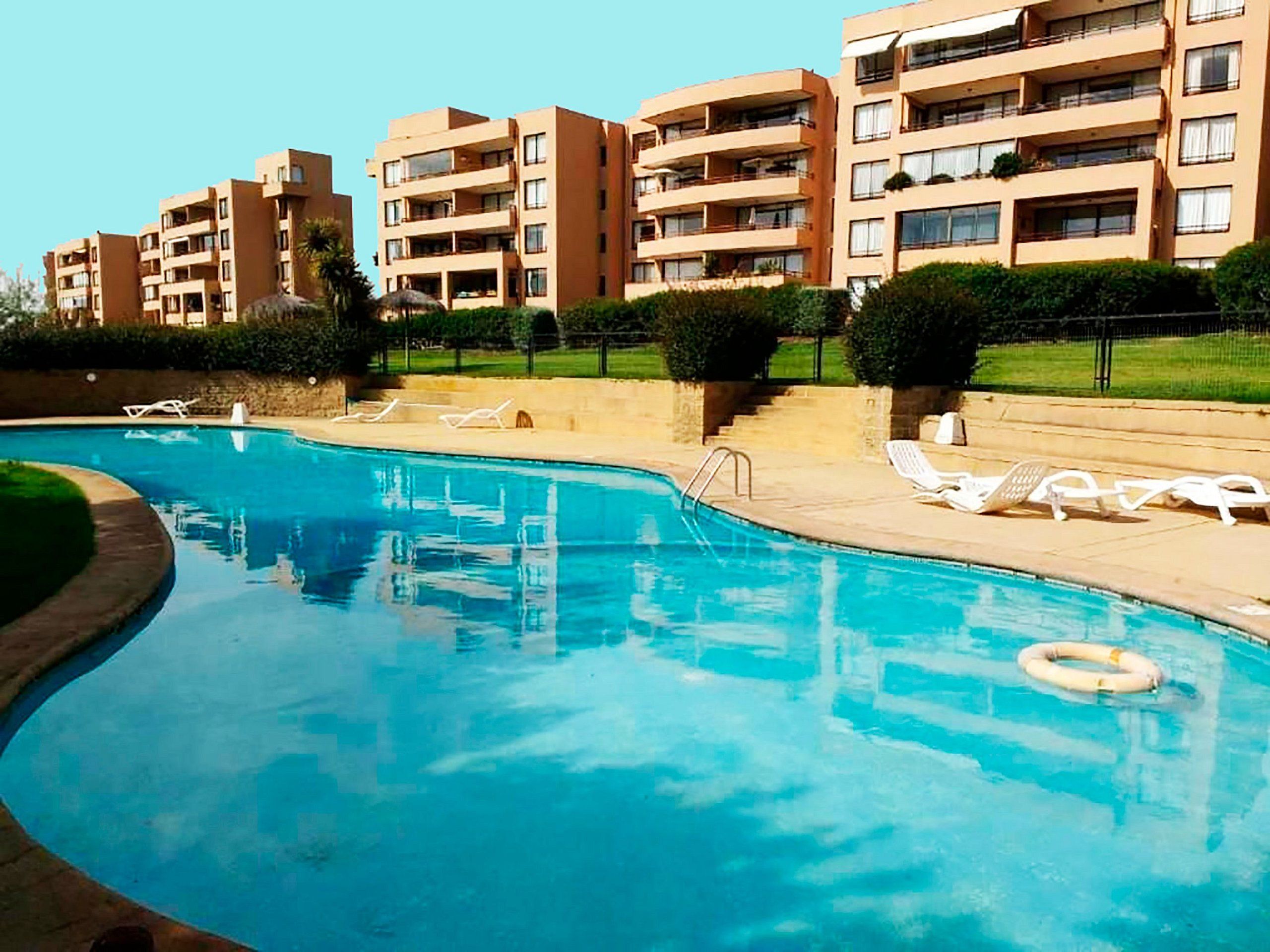 Una piscina con sillas de descanso y un flotador salvavidas, rodeada de edificios de apartamentos.