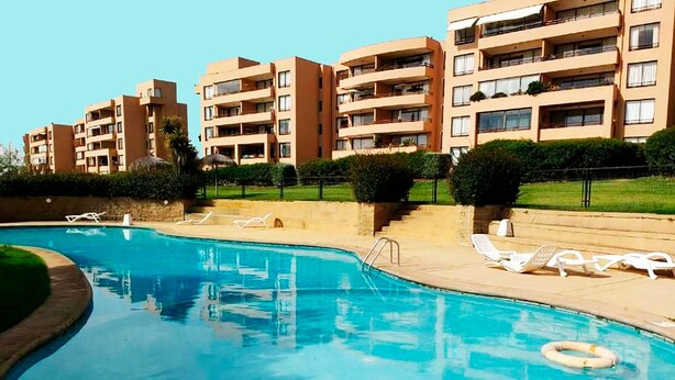 Una piscina con lettini e un galleggiante, circondata da palazzi.