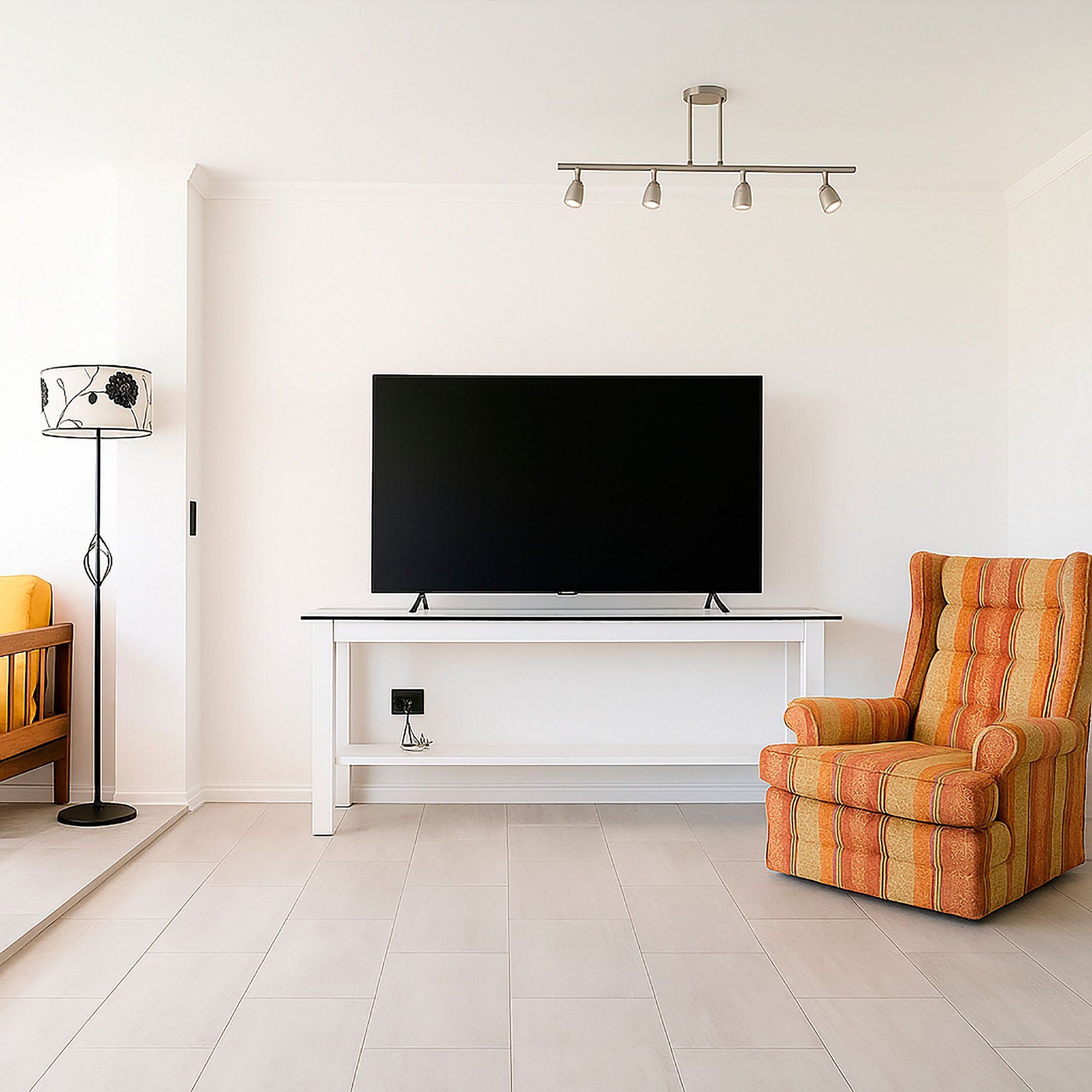 Una sala de estar con un televisor de pantalla plana sobre un soporte blanco, un sillón estampado y una lámpara de pie.