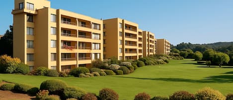 Un hotel de varios pisos con balcones, un césped cuidado y un campo de golf al fondo.