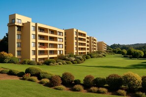 Een hotel met meerdere verdiepingen, балконы, een verzorgd gazon en een golfbaan op de achtergrond.