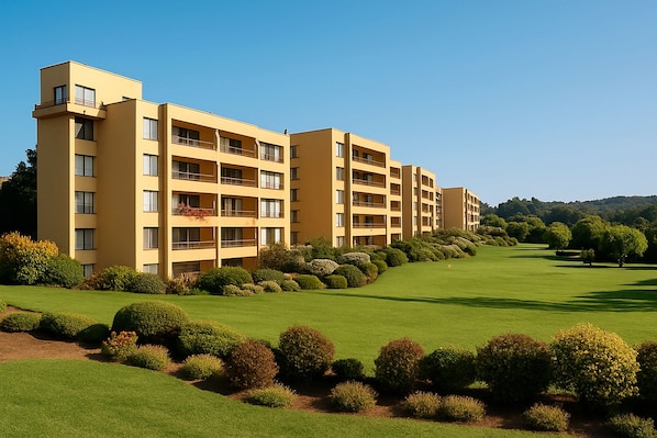 A multi-story hotel with balconies, a well-maintained lawn, and a golf course in the background.
