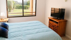 Una camera da letto con un letto, una televisione su un mobile in legno, una finestra vista verde e un comodino con una lampada.