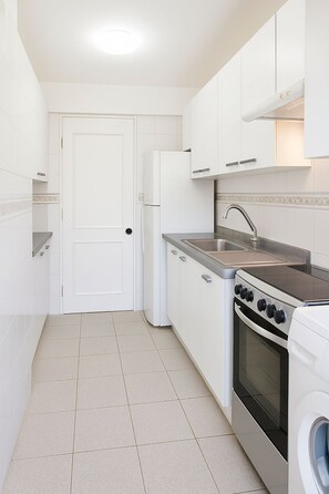 Een kleine keuken met witte kastjes, een roestvrijstalen spoelbak, een inbouwoven en een wasmachine.