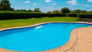 Una piscina blu cristallina con bordo curvo, circondata da un solarium in pietra e un prato ben curato.