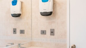 Un bagno con un lavandino bianco, mobili in legno scuro e due asciugamani ad aria montati a parete.