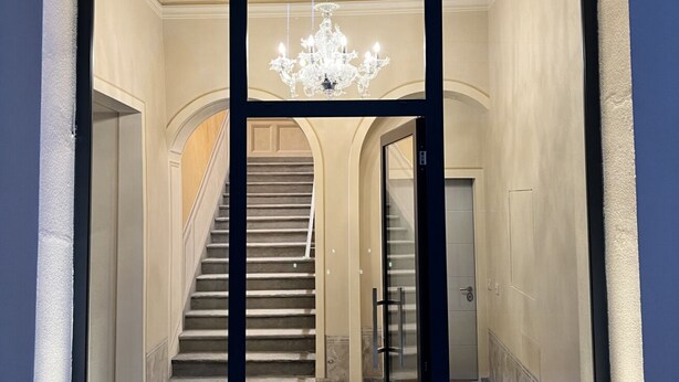 Un magnifique escalier, surmonté d’un lustre, mène à une porte dotée d’un panneau de verre.