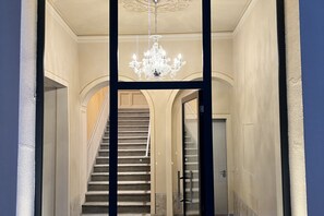 Una majestuosa escalera con una araña, que conduce a una puerta con un panel de vidrio.