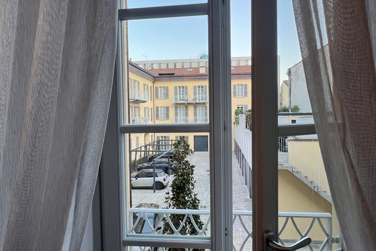 A view through a window with a balcony, a staircase, and a building with balconies and parked cars.