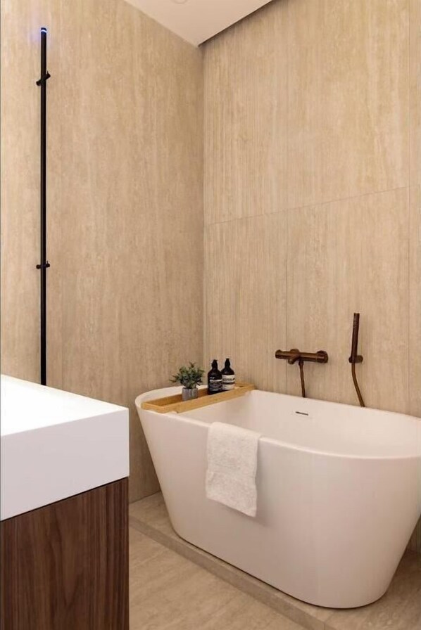 A modern bathroom with a freestanding bathtub, wooden side table, and a towel hanging on the tub.