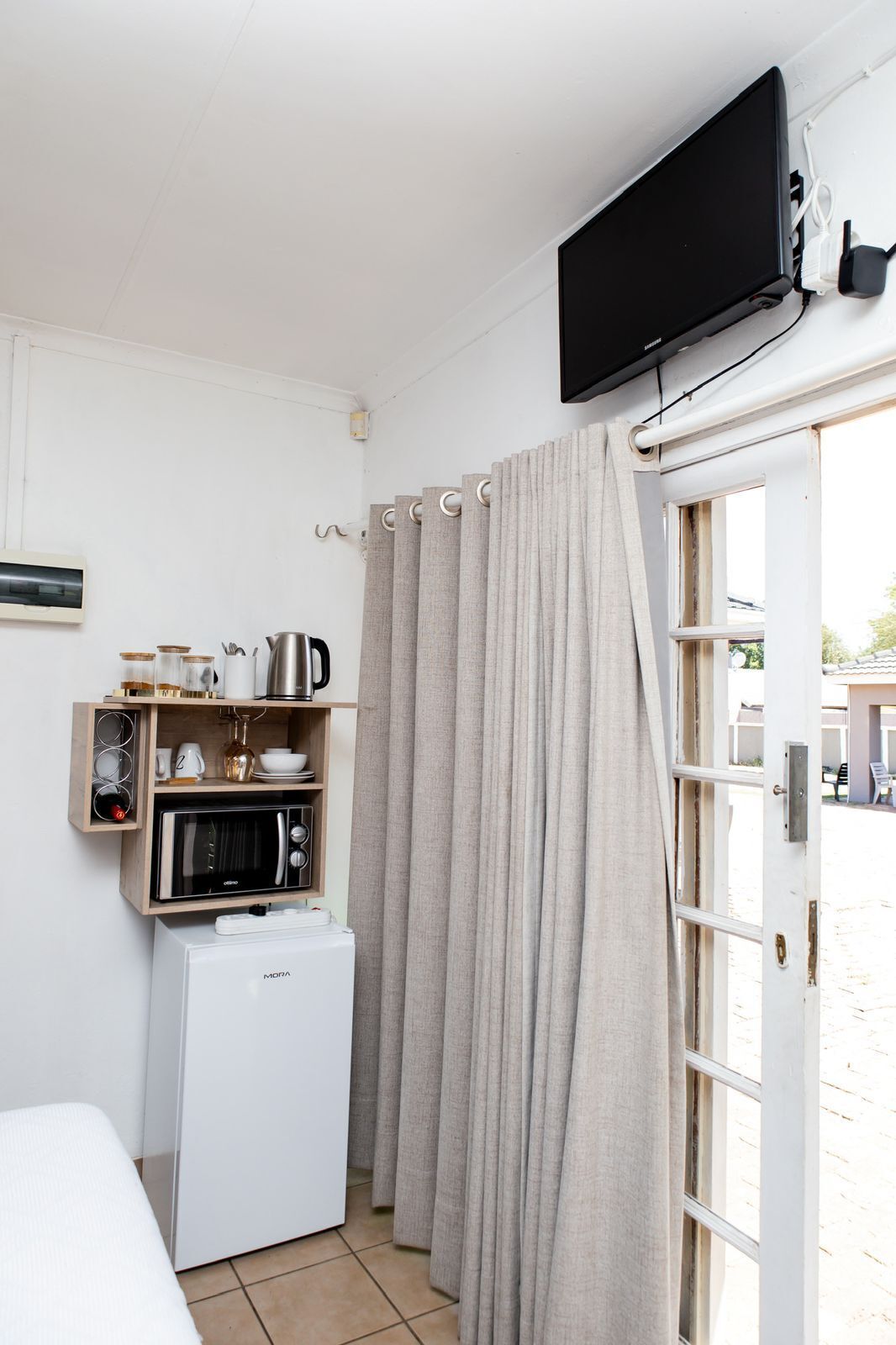 Ein gemütliches Zimmer mit einem Bett, einer Küchenzeile inklusive Mikrowelle, einem kleinen Kühlschrank und einem an der Wand befestigten Fernseher.