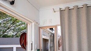 Une pièce comprenant un lit, un miroir, une porte donnant sur un espace extérieur avec une chaise, et une vue sur un bâtiment par la fenêtre.
