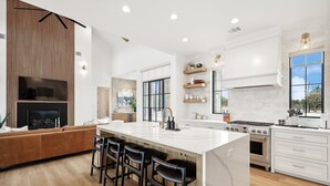Una cocina moderna con una isla grande, taburetes de bar, horno empotrado y un área de comedor con sofá.