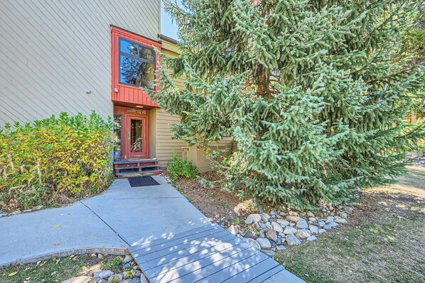 A residential building with a red door, a small porch, and a large evergreen tree in the front yard.