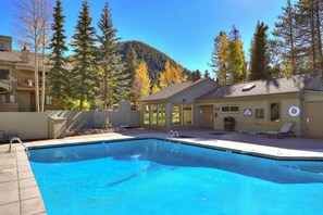 Un espace piscine doté d’une terrasse en bois, d’un poste de surveillance pour les sauveteurs et offrant une vue sur les montagnes en arrière-plan.