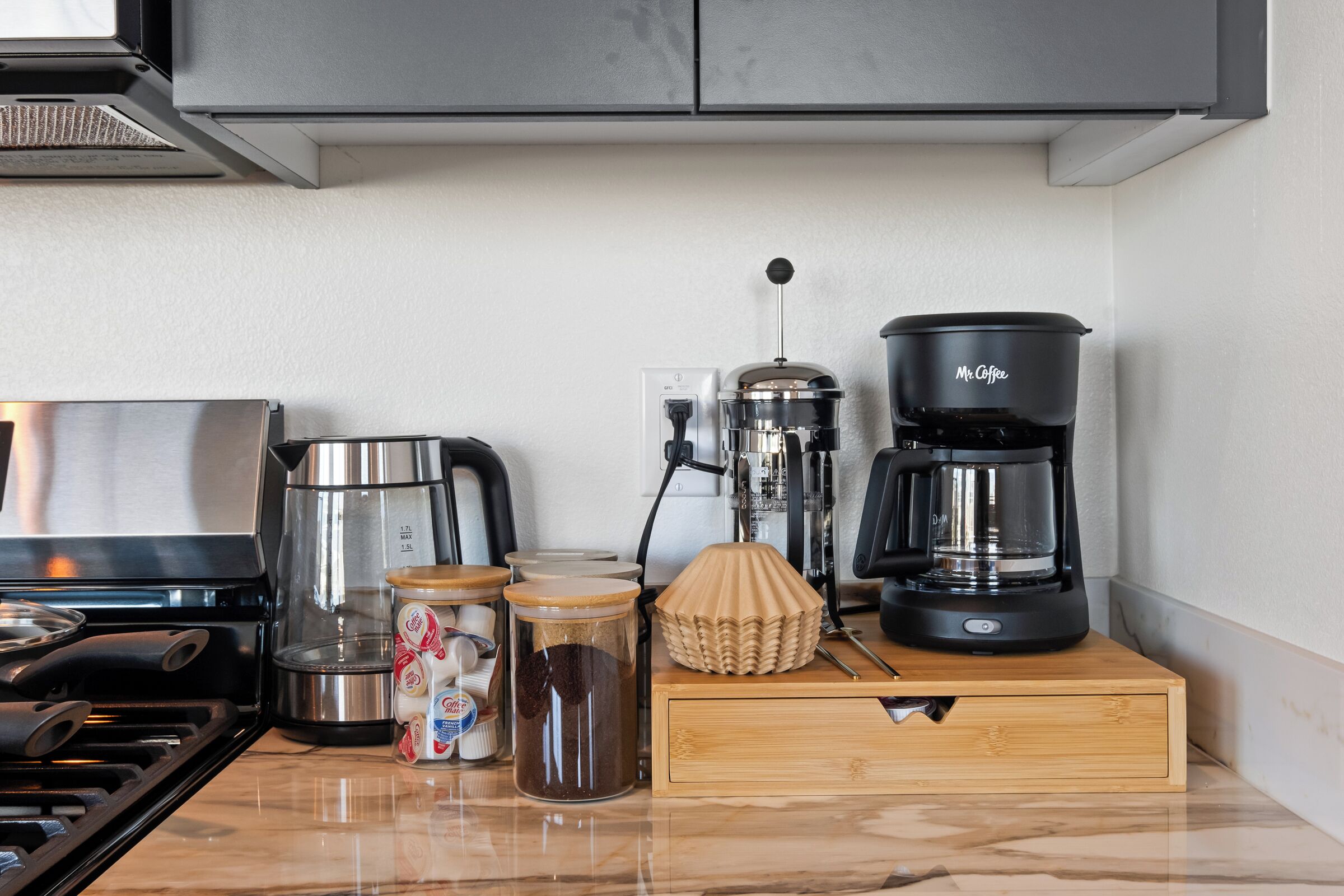 A kitchen with a stove, coffee maker, and various containers on the counter.