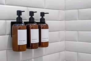 Drie flessen douchegel, shampoo en conditioner op een betegelde muur.