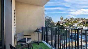 A balcony with a grill, chairs, and a view of a residential area.