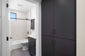 Een moderne badkamer met een witte betegelde wand, een badkuip, een toilet en donkergrijze kastjes.