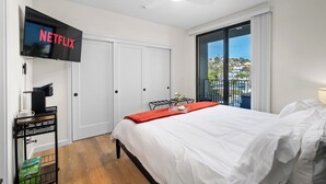Een moderne hotelkamer met een groot bed, een aan de muur bevestigde televisie, een koffiezetapparaat en uitzicht op de stad.