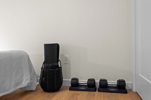 Un coin de pièce avec un lit, un tapis de sport noir et un ensemble d’haltères posés sur un support.