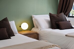 Een hotelkamer met twee bedden, elk voorzien van witte lakens en bruine kussens, een nachtkastje met een lamp, en een groene muur.
