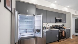 Een moderne keuken met grijze kastjes, een roestvrijstalen koelkast, een magnetron en een fornuis.