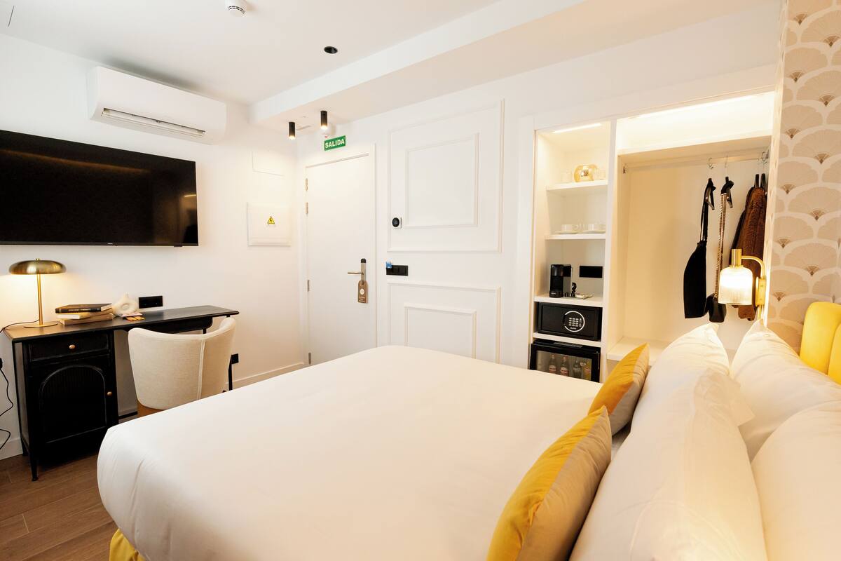 A hotel room with a bed, a desk, a chair, a TV, a wardrobe, and a bathroom with a towel rack.