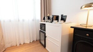 Une chambre d’hôtel équipée d’un minibar, d’un bureau avec un ordinateur, d’une lampe et d’une fenêtre avec des rideaux.