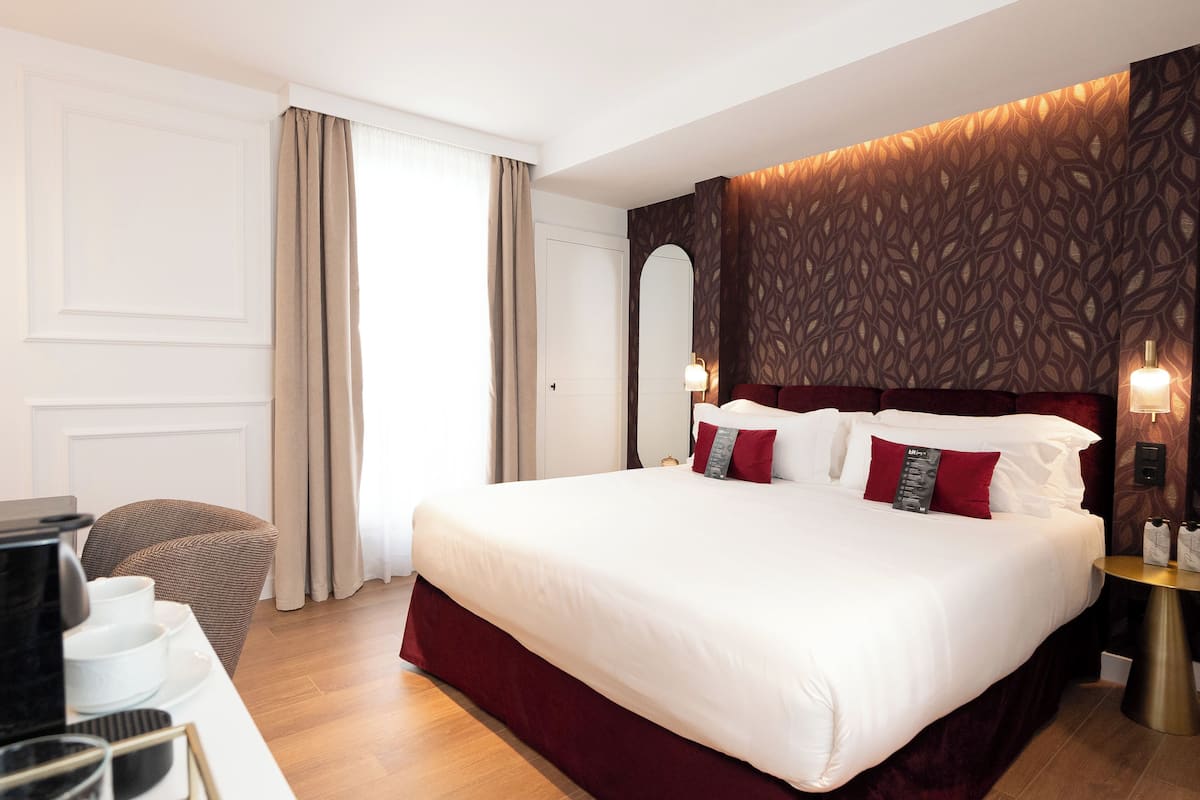 A hotel room with a large bed, a desk with a coffee maker, and a chair.