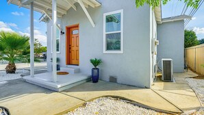 Uma casa térrea com varanda coberta, porta frontal e um pequeno jardim com uma palmeira e um vaso de planta.