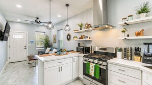 Uma cozinha moderna com armários brancos, eletrodomésticos de aço inoxidável e objetos decorativos nas prateleiras.