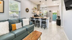 Uma cozinha moderna com banquetas, área de refeições com sofá e uma janela grande.