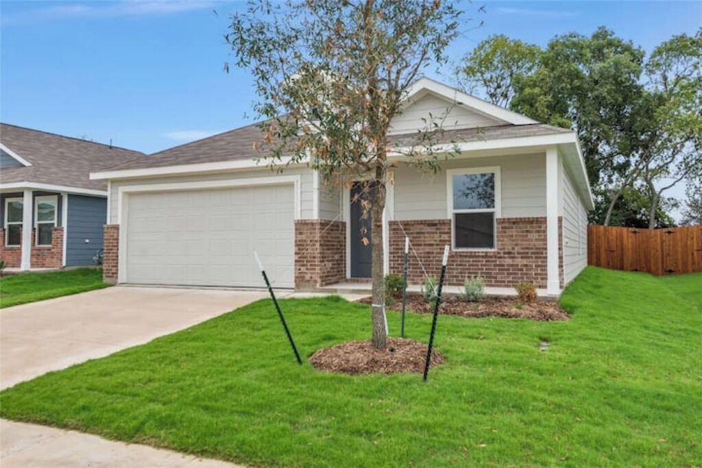 A single-story house with a garage, a small front yard with a young tree, and a wooden fence in the background.