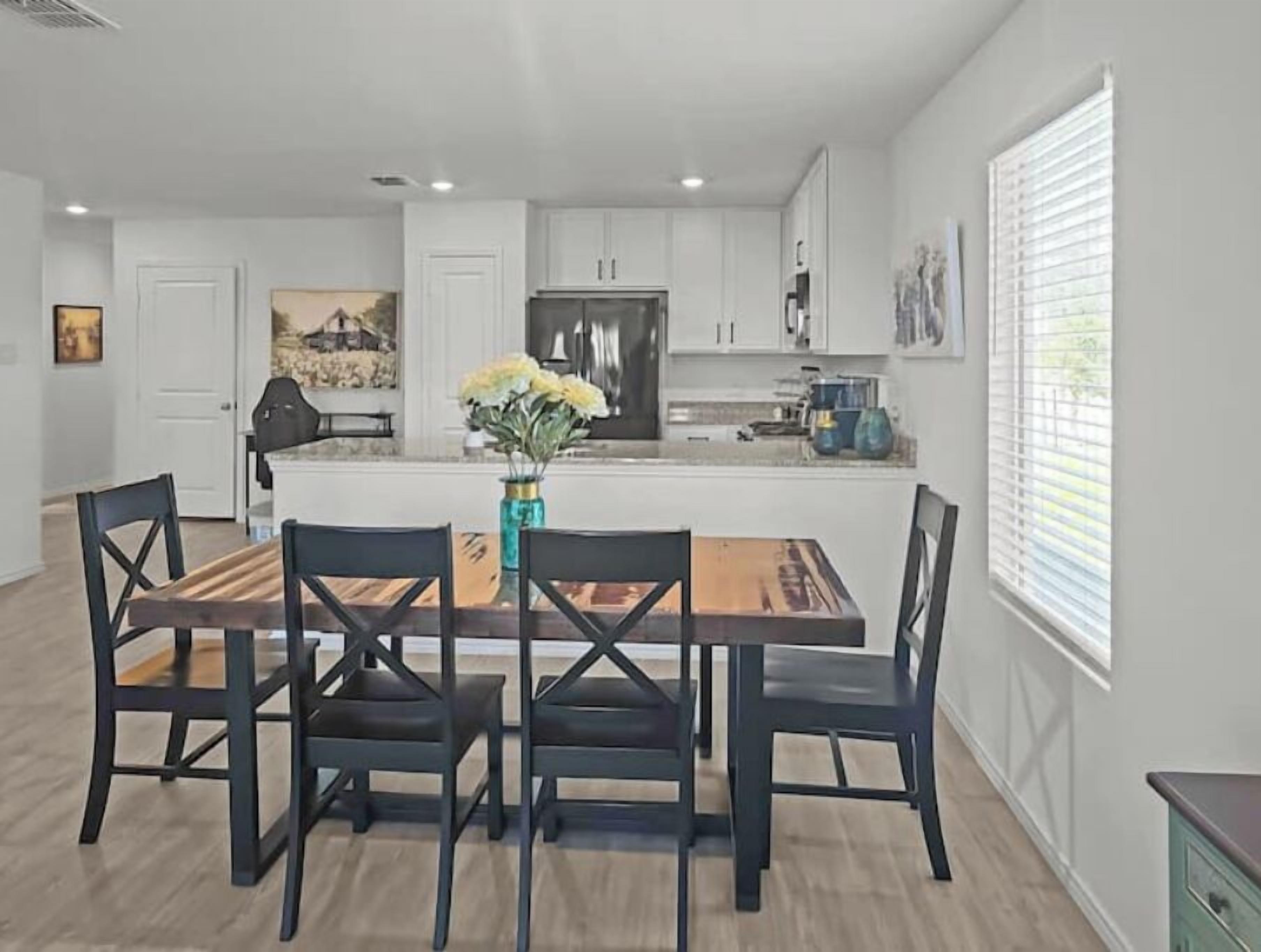A modern kitchen with white cabinets, a central island with a vase of flowers, and a dining area with four chairs.