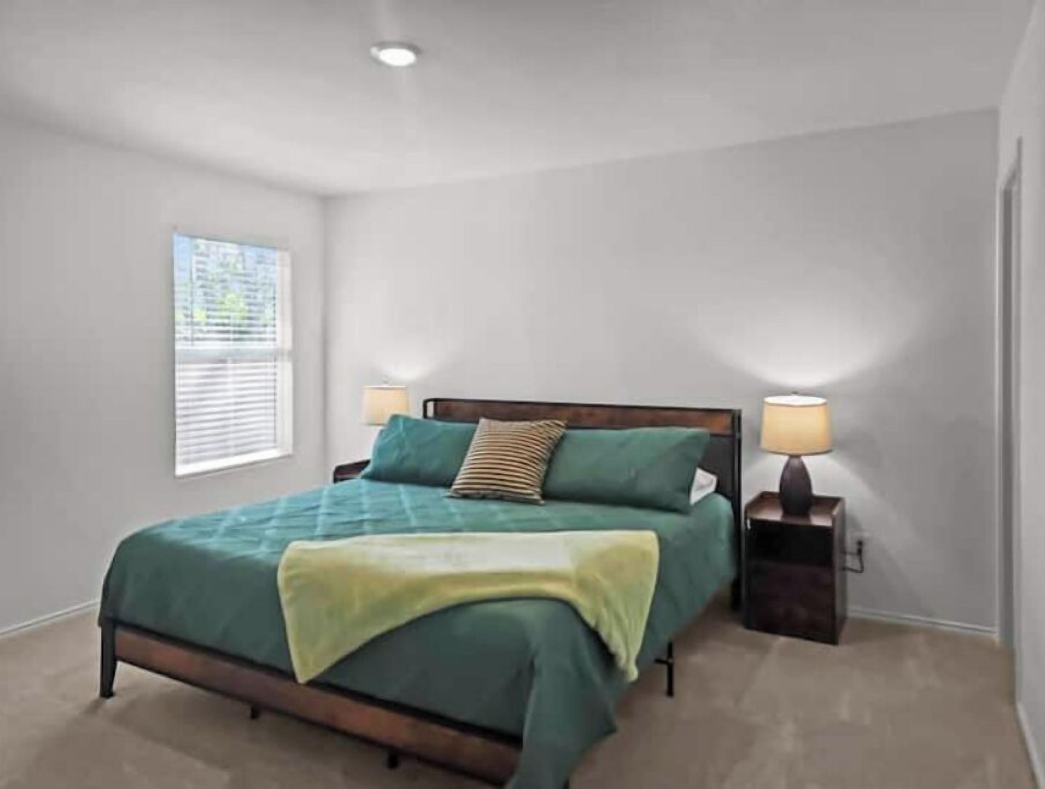 A bedroom with a bed, two bedside lamps, a window, and a ceiling light.