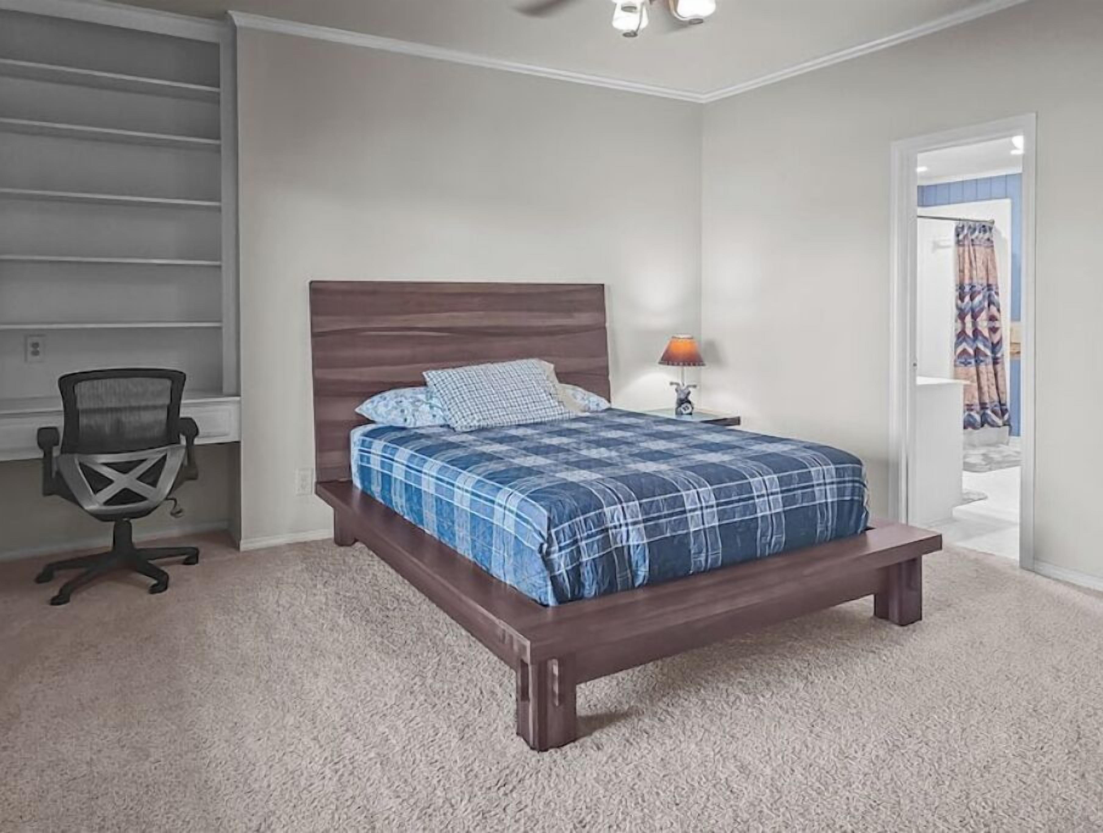 Une chambre à coucher avec un lit en bois, un bureau avec une chaise, une lampe et une porte donnant sur une autre pièce.