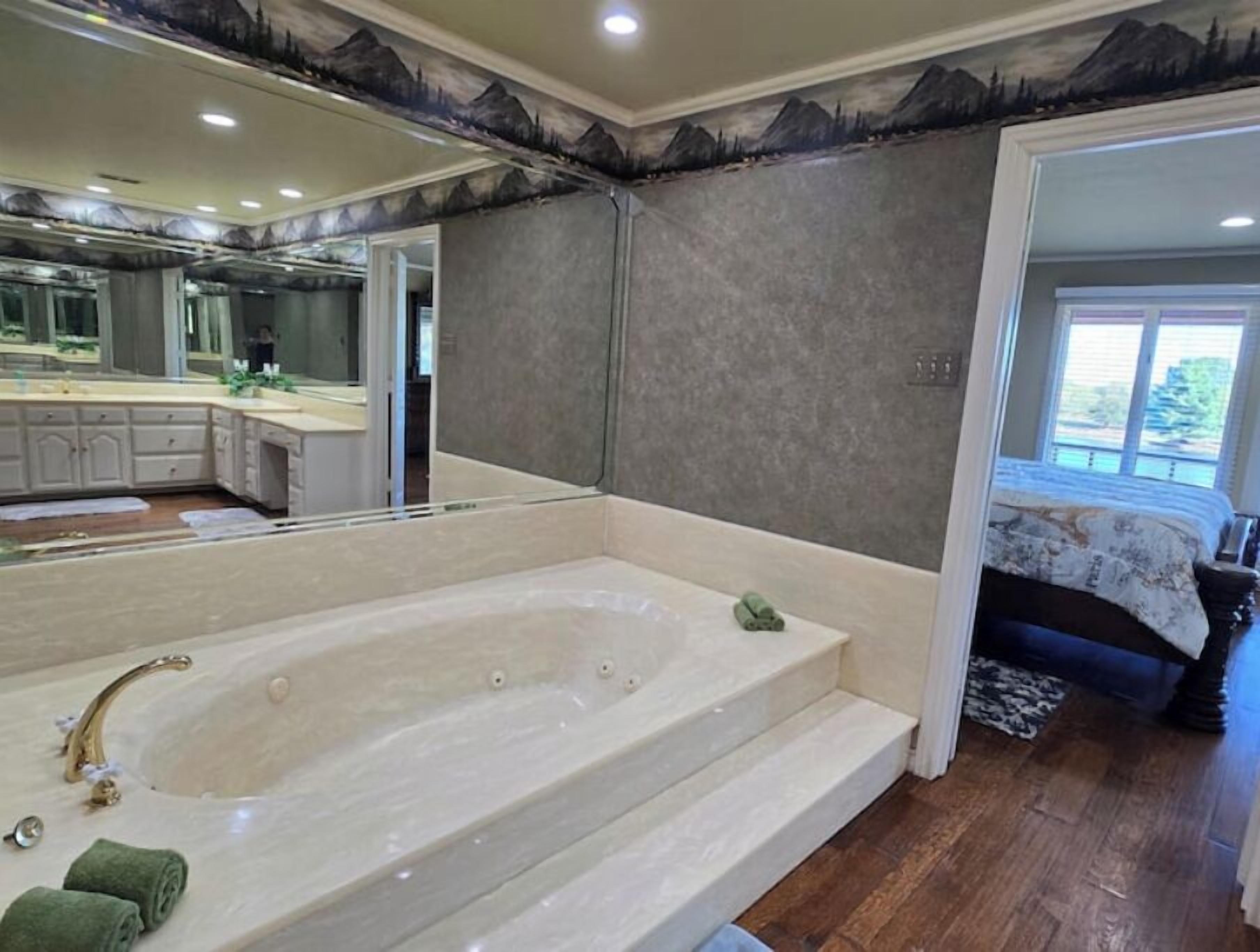 Une salle de bain avec une grande baignoire, un miroir et une vue sur une chambre à coucher avec un lit et une fenêtre.