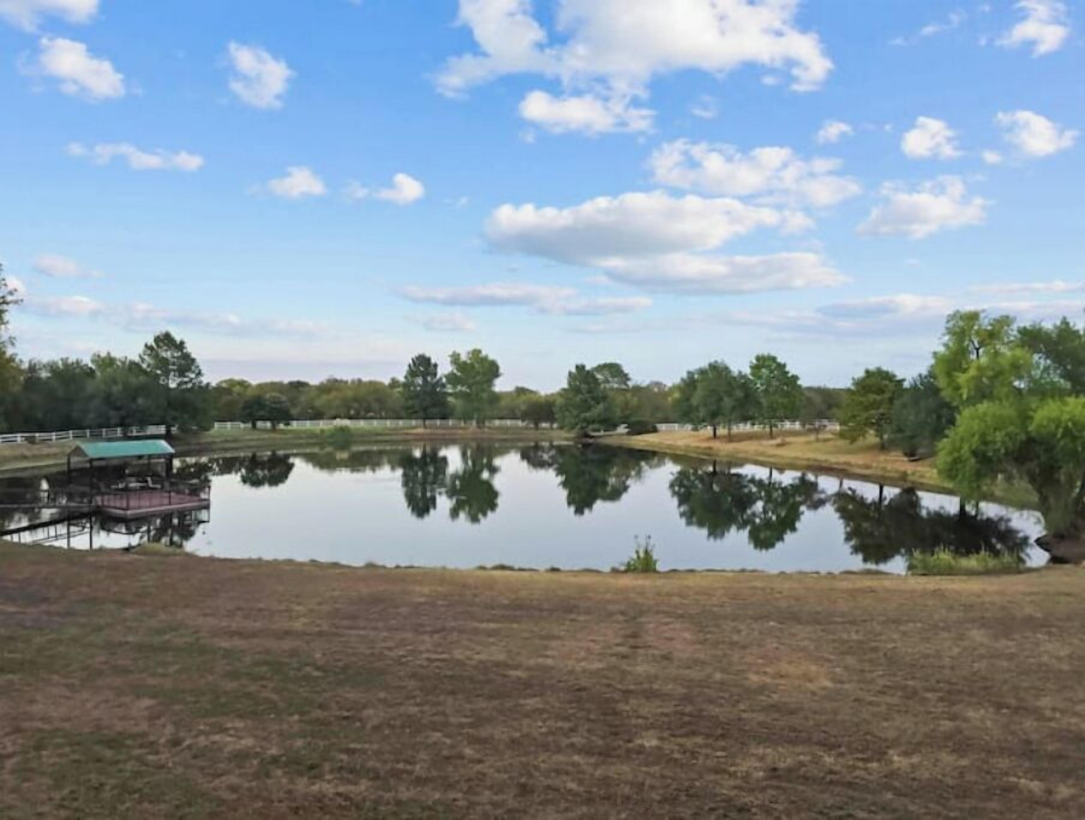 Un lac paisible, avec un quai et un petit bâtiment, entouré d’arbres et de vastes champs.