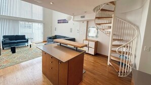 Ein modernes Wohnzimmer mit einem Holztisch, zwei Sofas, einer Wendeltreppe und einem großen Fenster, das für natürliches Licht sorgt.