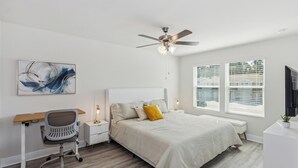 Een slaapkamer met een bed, een bureau, een stoel, een plafondventilator en een raam met jaloezieën.