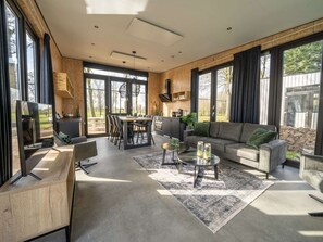 A modern living room with a sofa, coffee table, and dining area. - Modern Chalet by the River Maas (Kerkdriel)