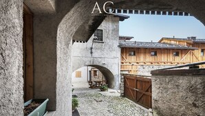Un patio con muros de piedra, un banco de madera y un edificio rústico al fondo.