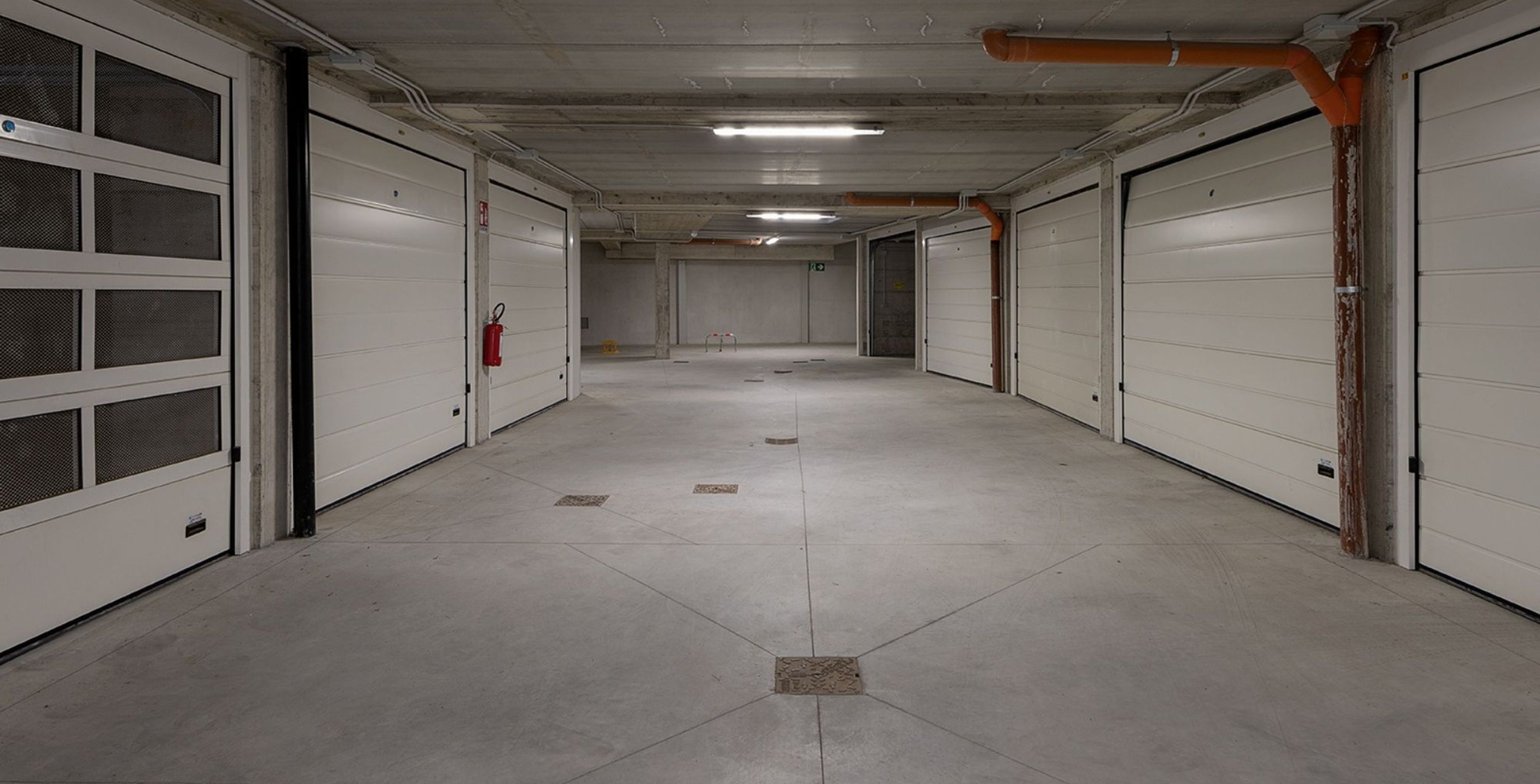 A long, empty corridor with white doors and a fire extinguisher on the left wall.