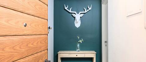 A wooden door with a mounted deer head, a small wooden table with a vase, and a teal wall.
